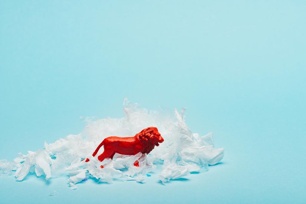 Red toy lion with plastic garbage on blue background, animal welfare concept - Photo, Image