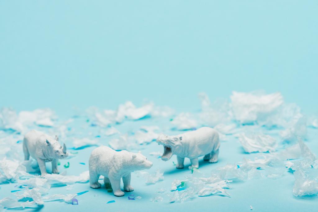Brinquedos brancos de hipopótamo, rinoceronte e urso com lixo de plástico no fundo azul, conceito de bem-estar animal
 - Foto, Imagem