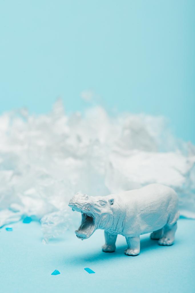 Enfoque selectivo del juguete hipopótamo con basura plástica sobre fondo azul, concepto de bienestar animal
 - Foto, imagen