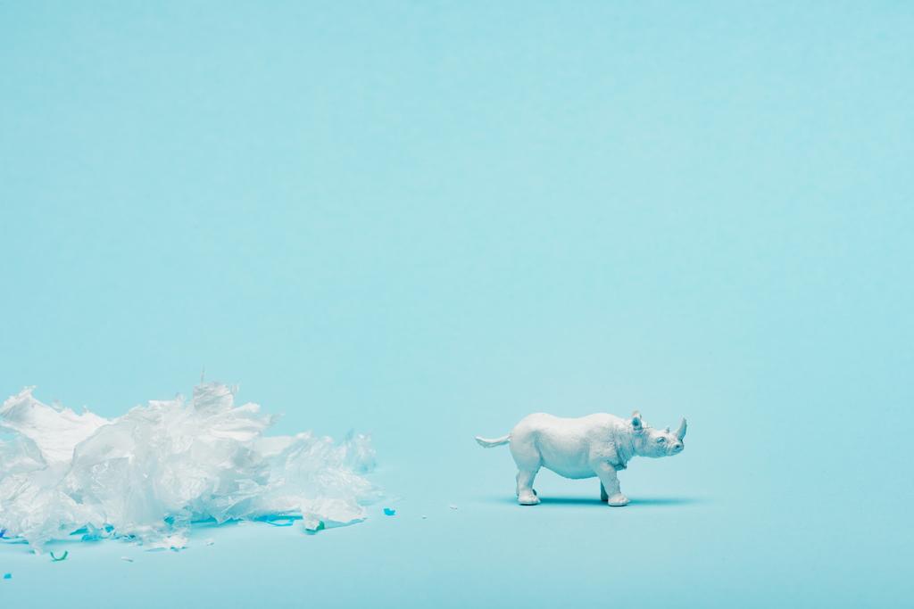 青い背景に白いサイのおもちゃとプラスチックごみ、動物福祉の概念 - 写真・画像