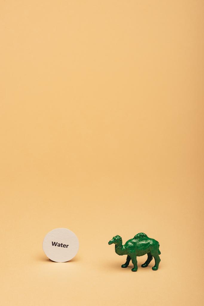 Camelo de brinquedo verde com água lettering no cartão no fundo amarelo, conceito de escassez de água
 - Foto, Imagem