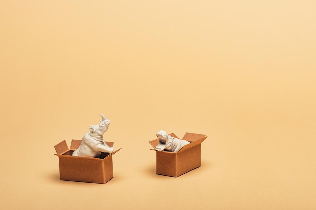 Hippopotame jouet blanc et rhinocéros dans des boîtes en carton sur fond jaune, concept de bien-être animal
 - Photo, image