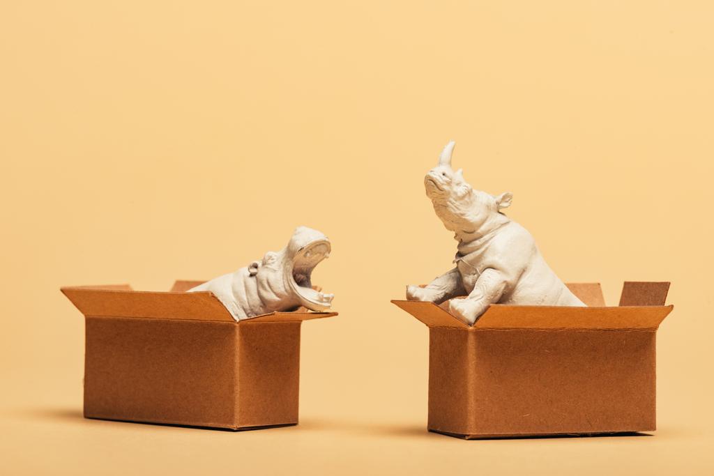 Witte speelgoed nijlpaard en neushoorn in kartonnen dozen op gele achtergrond, dierenwelzijn concept - Foto, afbeelding