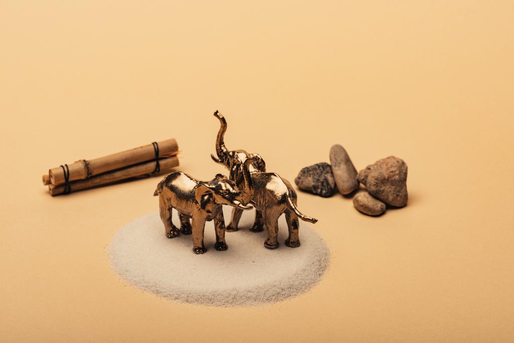 Elefantes de juguete sobre arena con piedras y palos de madera sobre fondo amarillo, concepto de bienestar animal
 - Foto, imagen