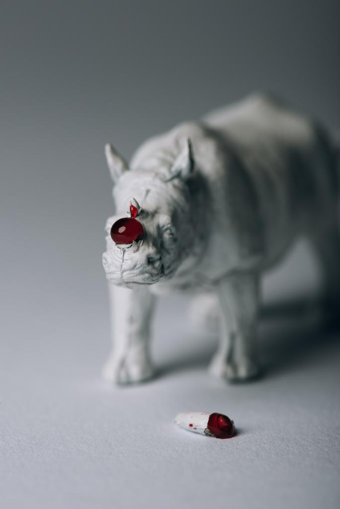 Рог с кровью и игрушечными носорогами на сером фоне, охота за концепцией рога
 - Фото, изображение