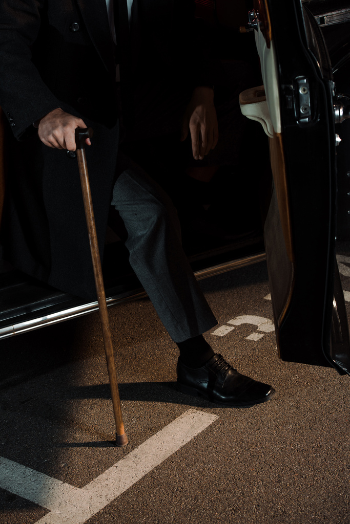 przycięty widok gangstera trzymającego laskę w pobliżu samochodu retro z otwartymi drzwiami samochodu  - Zdjęcie, obraz