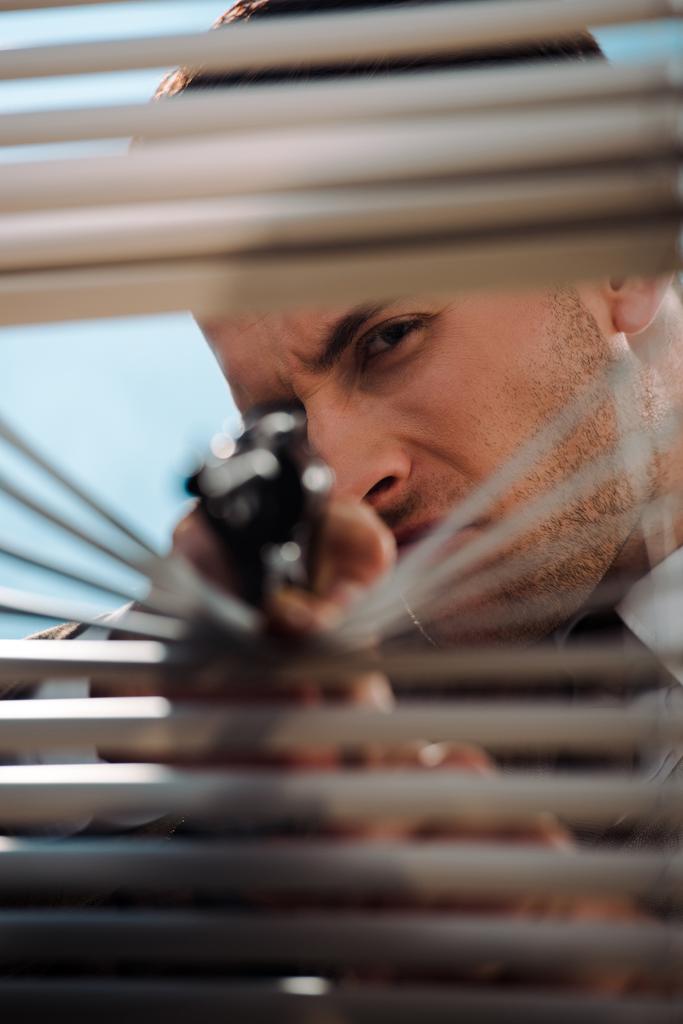 szelektív fókusz veszélyes ember kezében pisztoly közelében ablak redőny - Fotó, kép
