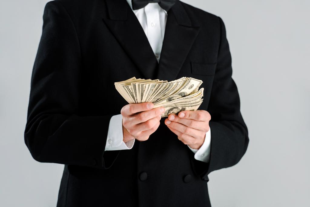 καλλιεργημένη άποψη του πλουσίου με κοστούμι που κρατά τραπεζογραμμάτια δολαρίου απομονωμένα σε γκρι  - Φωτογραφία, εικόνα