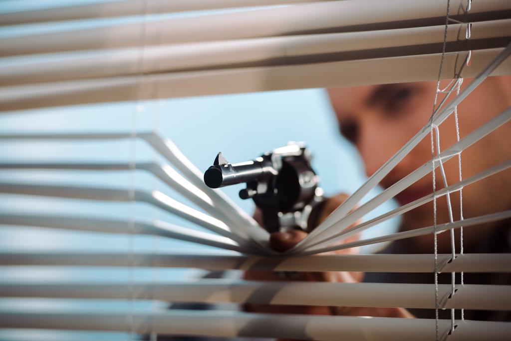 panoramatický záběr černé pistole v blízkosti žaluzií v ruce gangstera  - Fotografie, Obrázek