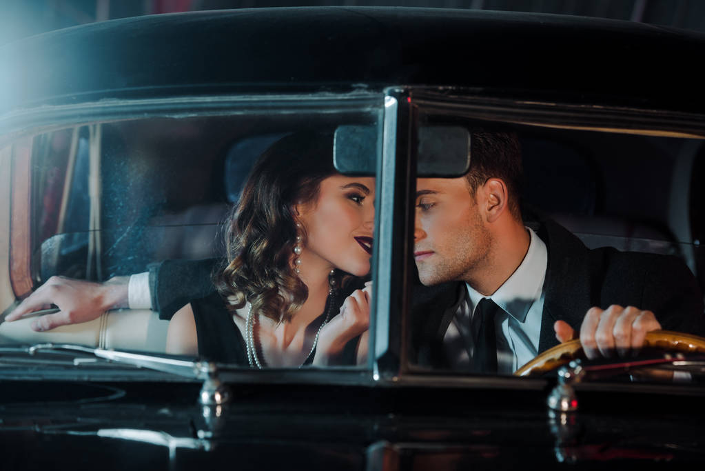 szelektív fókusz jóképű férfi és boldog nő ül retro autó  - Fotó, kép