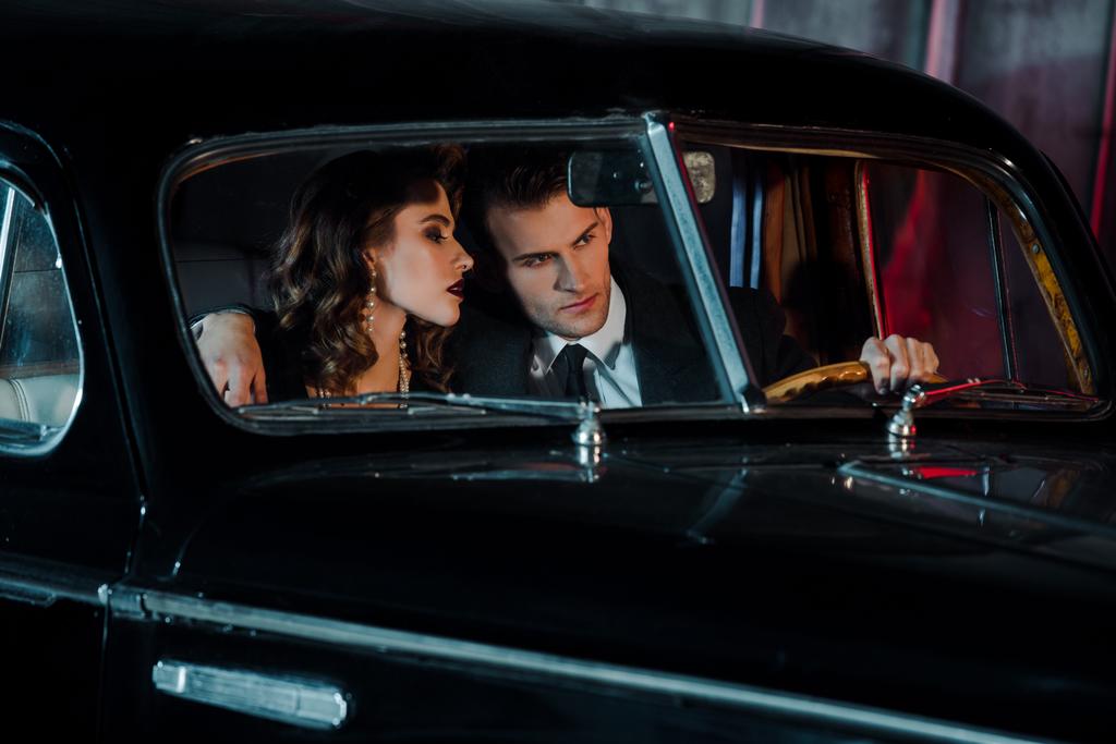 επιλεκτική εστίαση του άνδρα αγγίζοντας τιμόνι και κάθεται κοντά ελκυστική γυναίκα σε ρετρό αυτοκίνητο  - Φωτογραφία, εικόνα