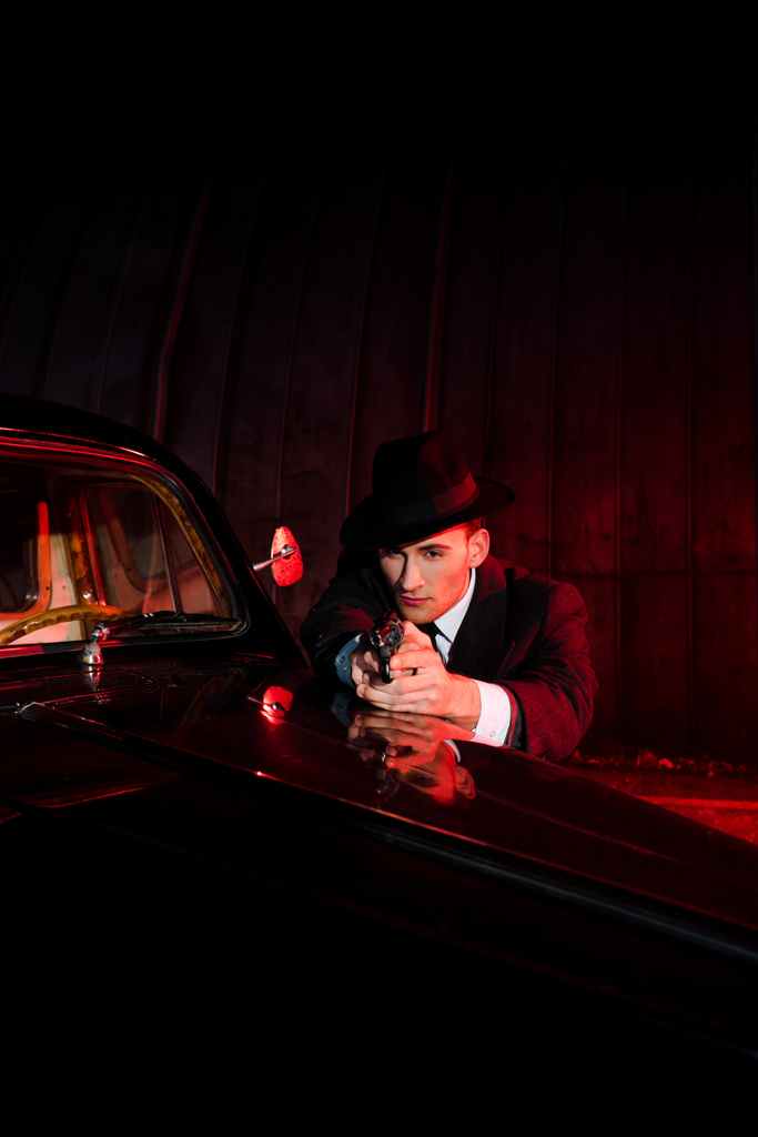 bel homme au chapeau tenant pistolet près de voiture vintage et noire
  - Photo, image