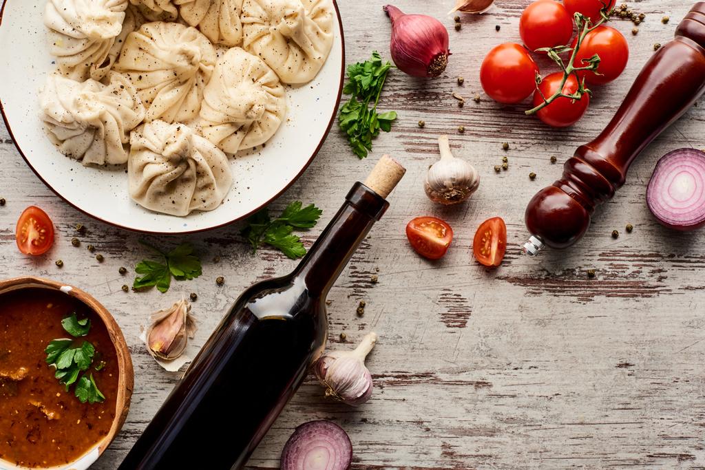 bovenaanzicht van heerlijke khinkali bij fles wijn, kharcho, groenten en specerijen op houten tafel - Foto, afbeelding