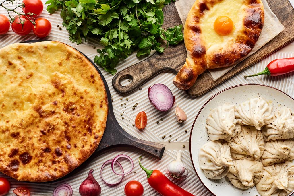 top view of delicious khinkali and khachapuri near vegetables and spices on beige textured background - Photo, Image