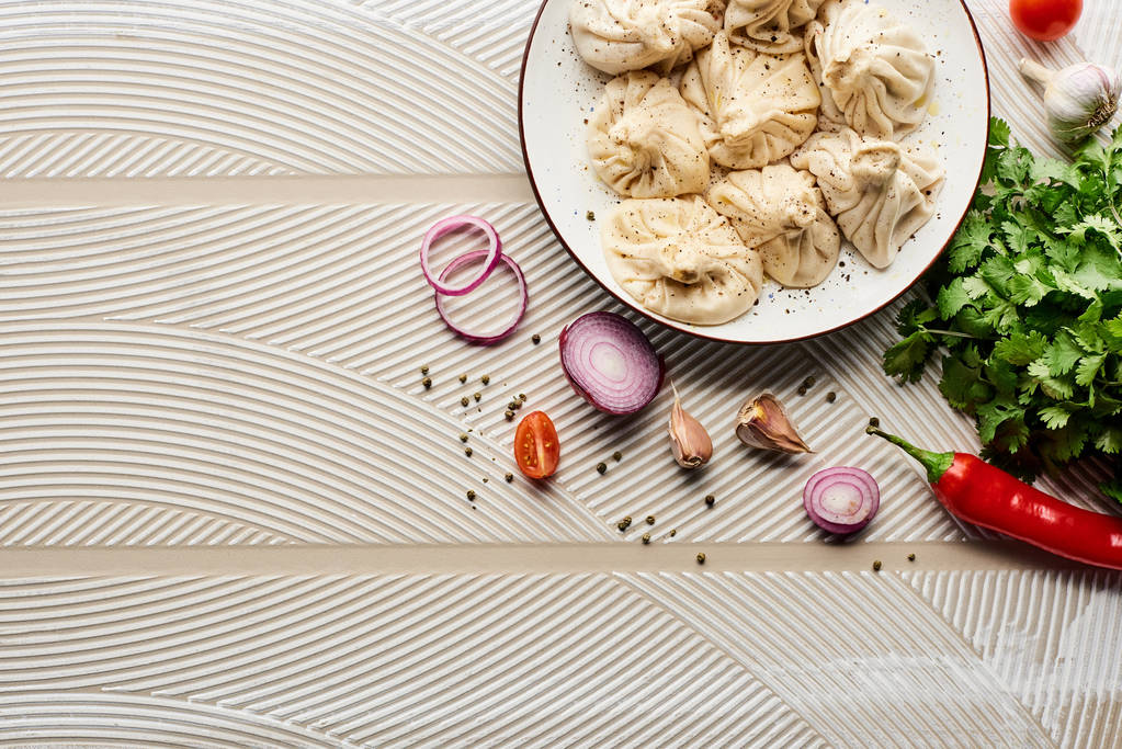 vrchol pohled na lahodné khinkali v blízkosti zeleniny a koření na béžové texturované pozadí - Fotografie, Obrázek