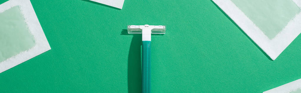 vista superior de la maquinilla de afeitar desechable verde y rayas de cera depilación sobre fondo verde, plano panorámico
 - Foto, Imagen