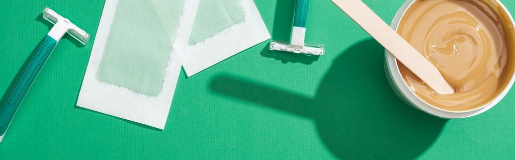 vista superior de maquinillas de afeitar desechables verdes, cera y rayas de depilación sobre fondo verde, plano panorámico
 - Foto, Imagen