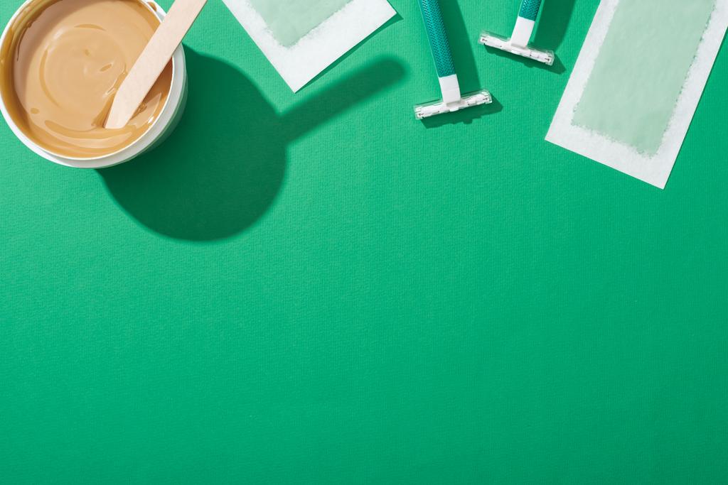 vista superior de afeitadoras desechables verdes, cera y rayas de depilación sobre fondo verde
 - Foto, imagen