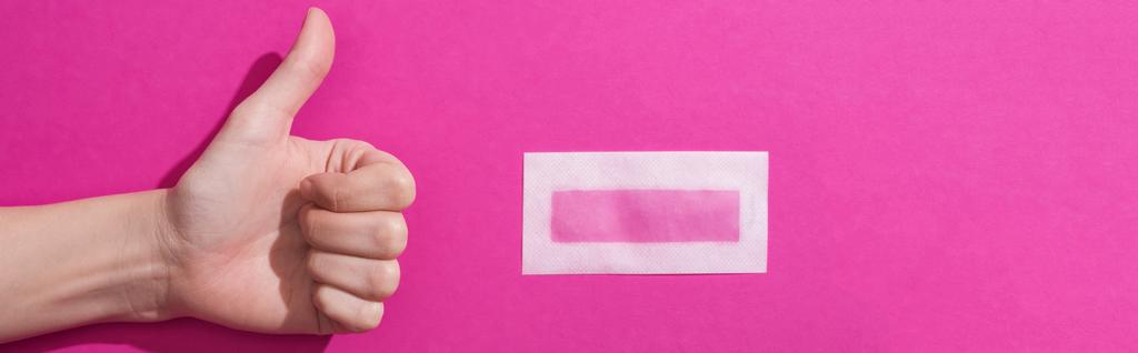 ピンクの背景に剥き出しのワックスのストライプの近くに親指を示す女性のクロップドビュー,パノラマショット - 写真・画像