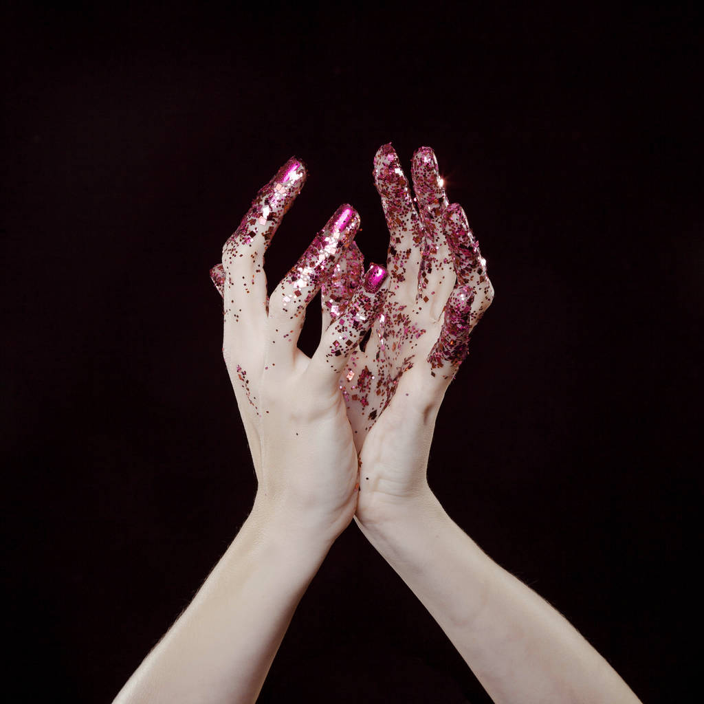 mooie vrouw handen met roze glitter in de voorkant van zwarte achtergrond - Foto, afbeelding