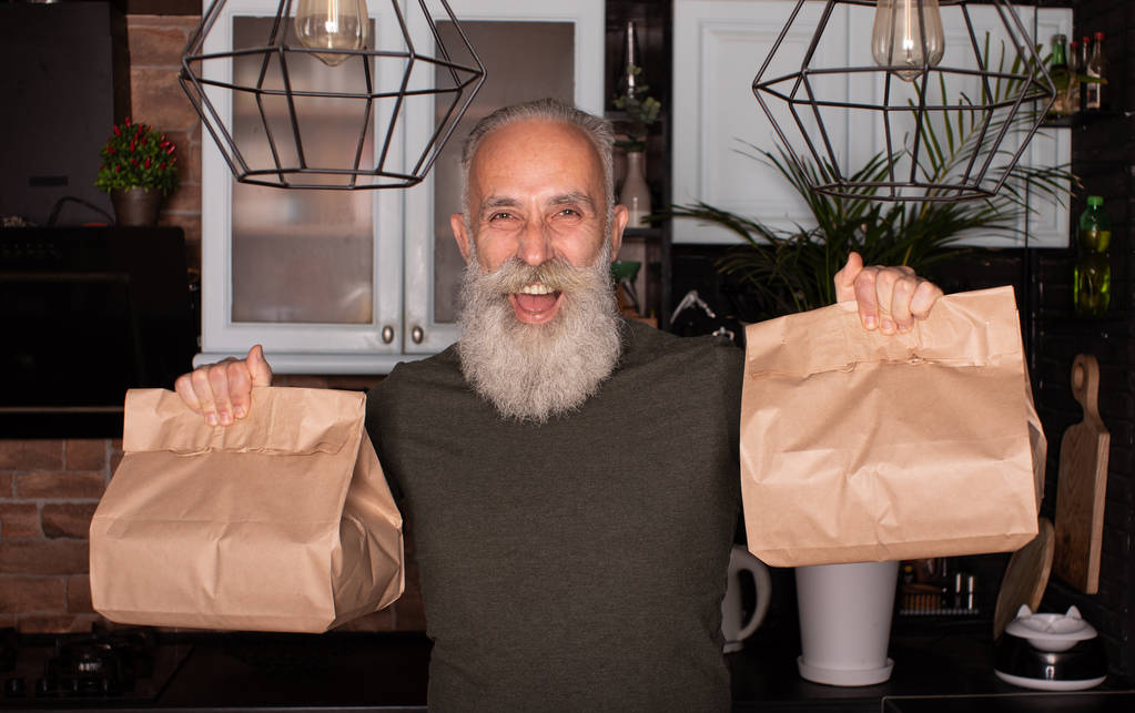 Concetto di consegna. Buon uomo anziano barbuto consegna cibo in sacchetto di carta usa e getta a casa del cliente
. - Foto, immagini