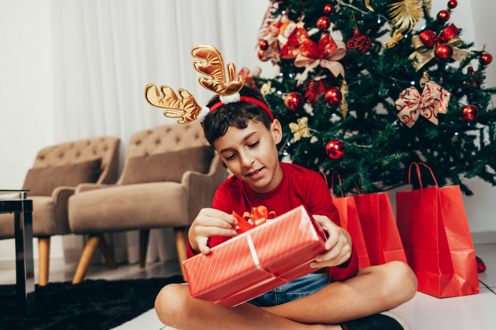 Χαρούμενο και αστείο μικρό αγόρι με δώρα και καλά Χριστούγεννα δέντρο. Καλά Χριστούγεννα και νέο έτος έννοια. - Φωτογραφία, εικόνα