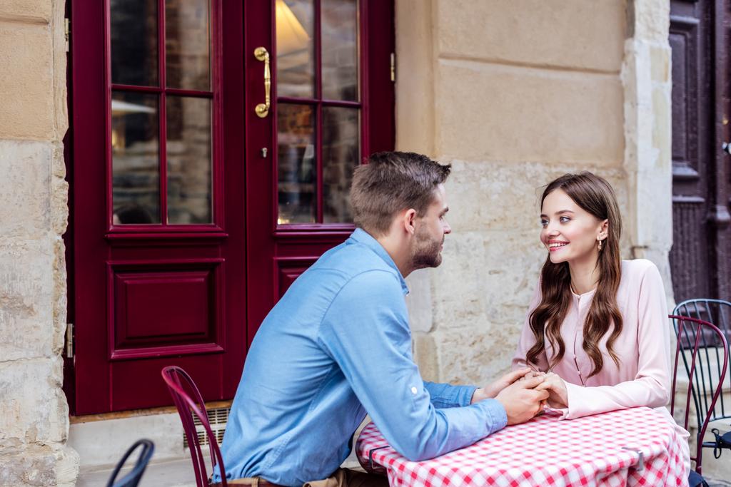 gelukkig jong paar vasthouden handen en kijken naar elkaar terwijl zitten in de straat cafe - Foto, afbeelding