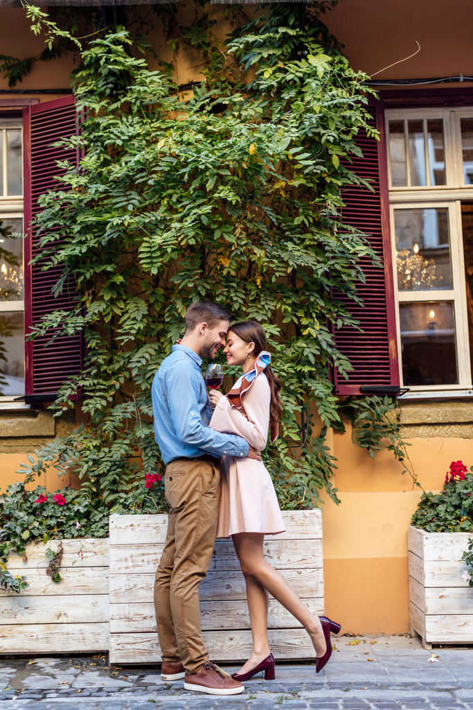 vista lateral do feliz casal jovem abraçando enquanto estava perto de casa coberta com hera verde
 - Foto, Imagem