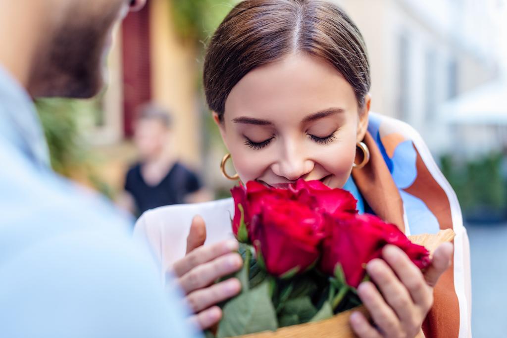 Ausgeschnittene Ansicht eines jungen Mannes, der seiner glücklichen Freundin auf der Straße einen Strauß Rosen überreicht - Foto, Bild