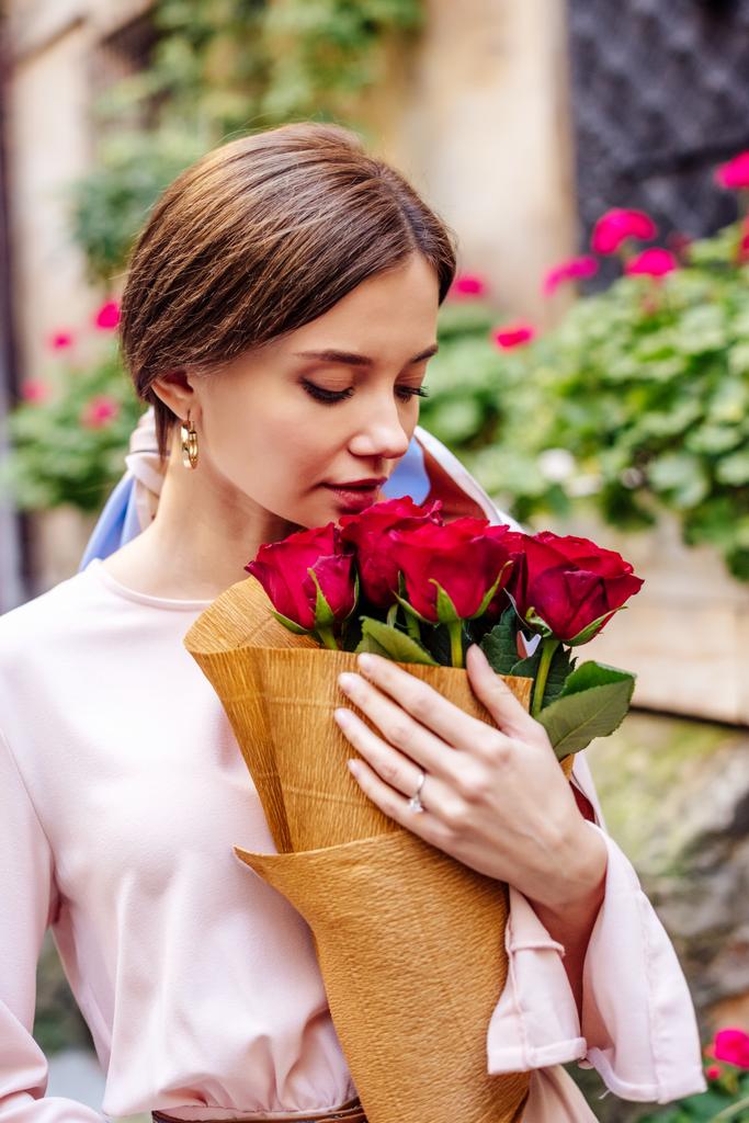 schöne, verträumte Mädchen genießen Geschmack der roten Rosen, während sie Blumenstrauß halten - Foto, Bild