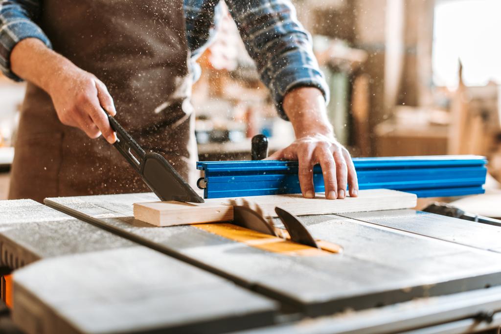 selective focus of woodworker holding plank near circular saw - Photo, Image
