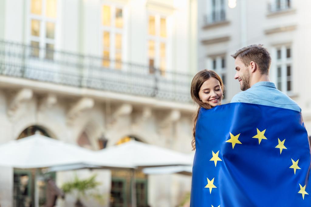 giovane, sorridente coppia di turisti avvolgente nella bandiera del sindacato europeo sulla strada
 - Foto, immagini