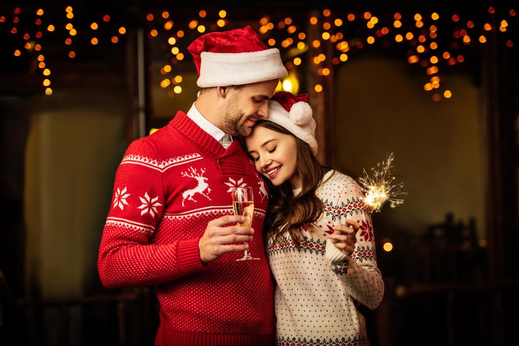 Улыбающийся мужчина с бокалом шампанского обнимает счастливую девушку, держа искру
 - Фото, изображение