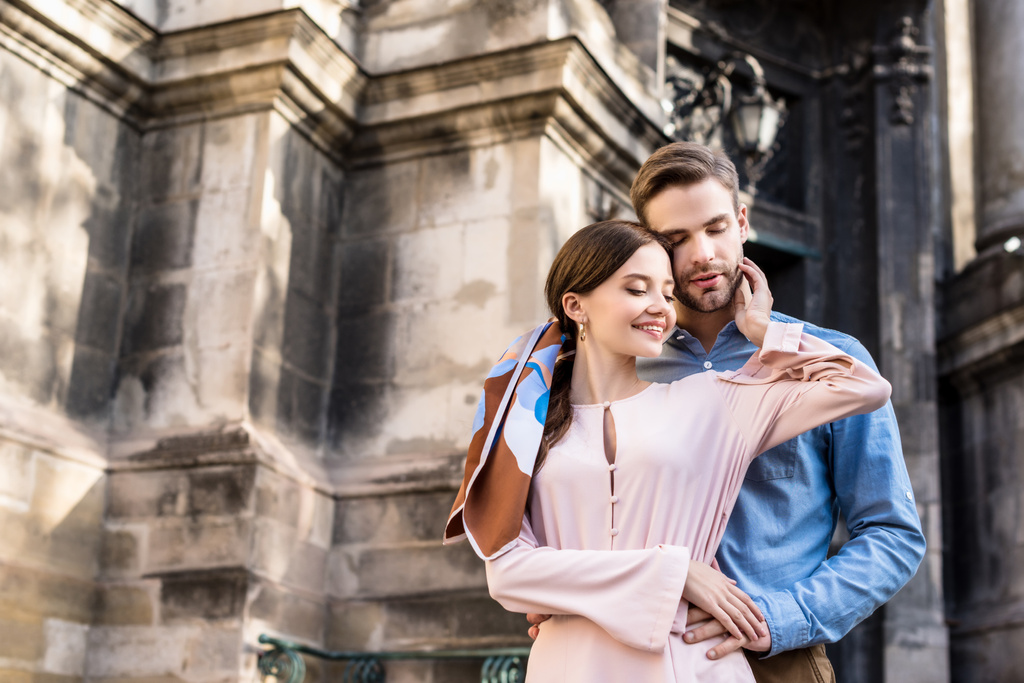 happy, stylish couple embracing with closed eyes while standing on street - Photo, Image