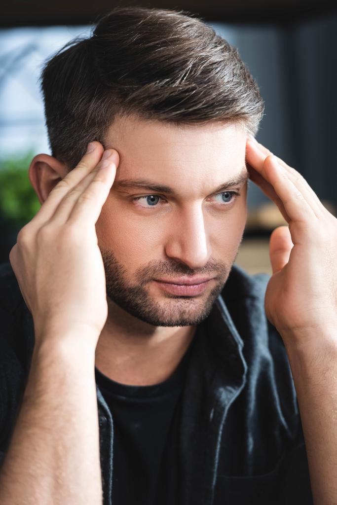 handsome man with headache touching head and looking away in apartment  - Photo, Image