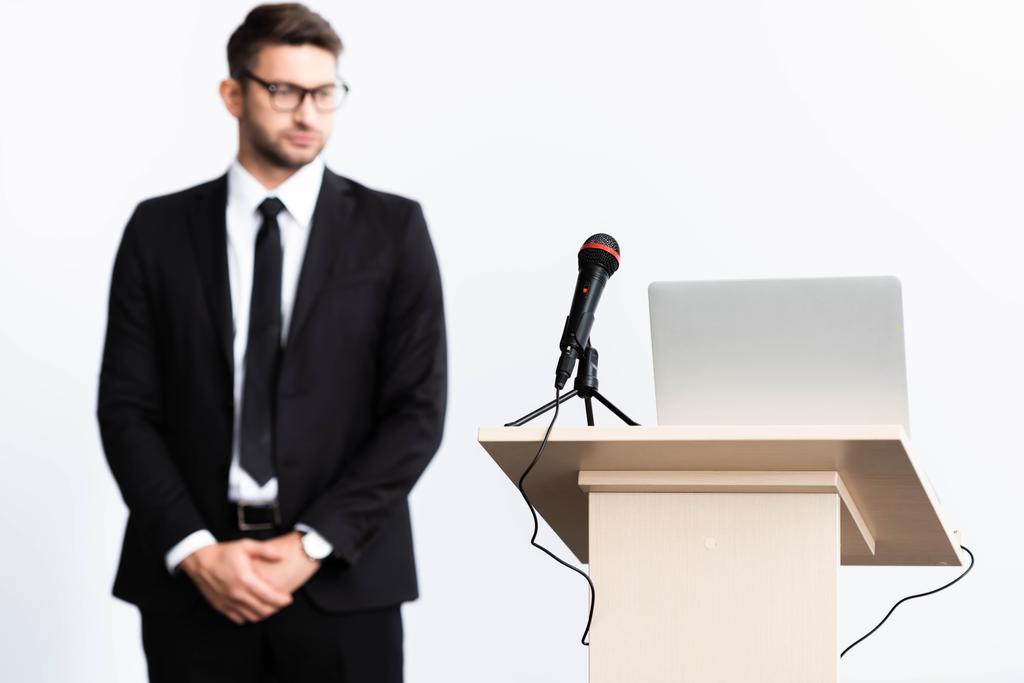 избирательный фокус трибуны подиума с ноутбуком и микрофоном, бизнесмен в костюме на фоне изолированного на белом фоне
 - Фото, изображение