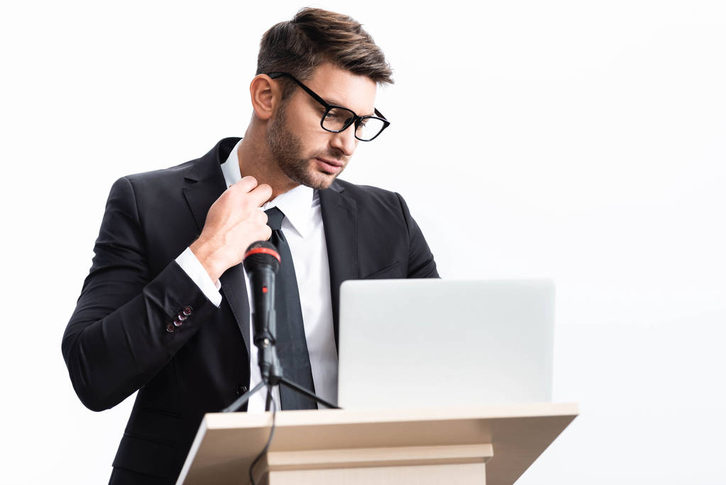 підкреслений бізнесмен у костюмі стоїть на подіумній трибуні і дивиться на ноутбук під час конференції ізольовано на білому
 - Фото, зображення
