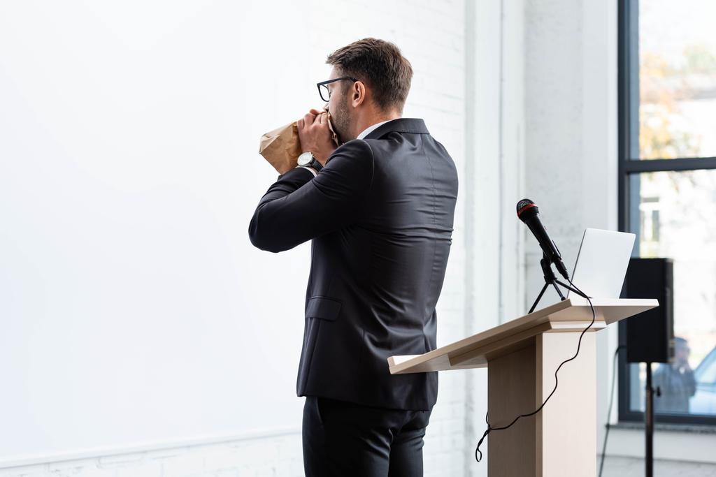 Rückansicht eines verängstigten Geschäftsmannes im Anzug, der während einer Konferenz Papiertüten einatmet - Foto, Bild