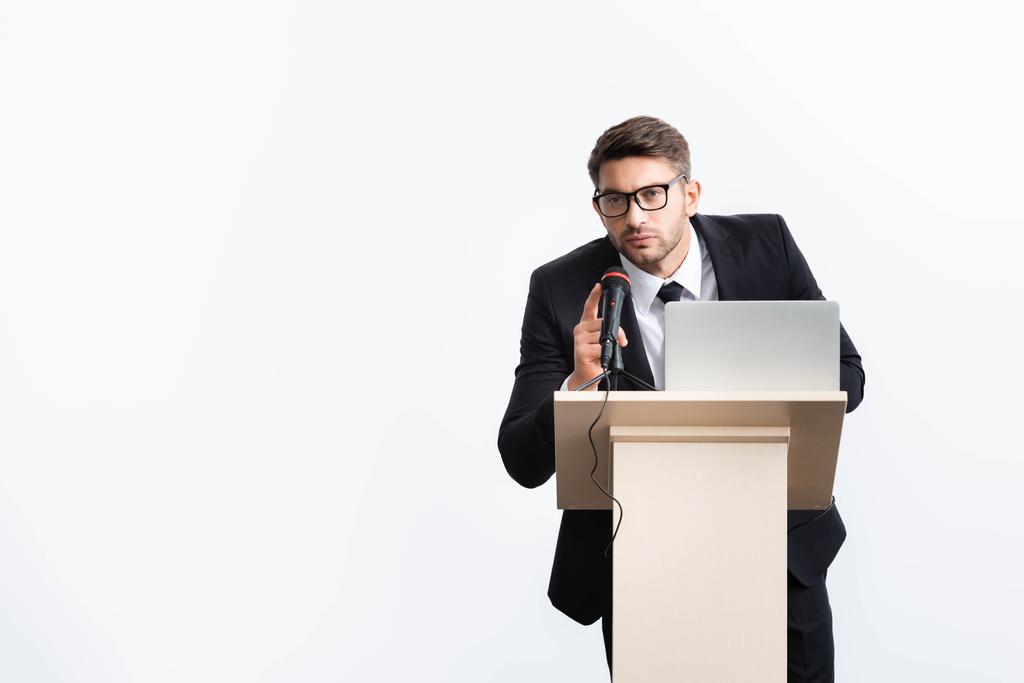homem de negócios de terno em pé no tribuno pódio e falando durante conferência isolada em branco
  - Foto, Imagem