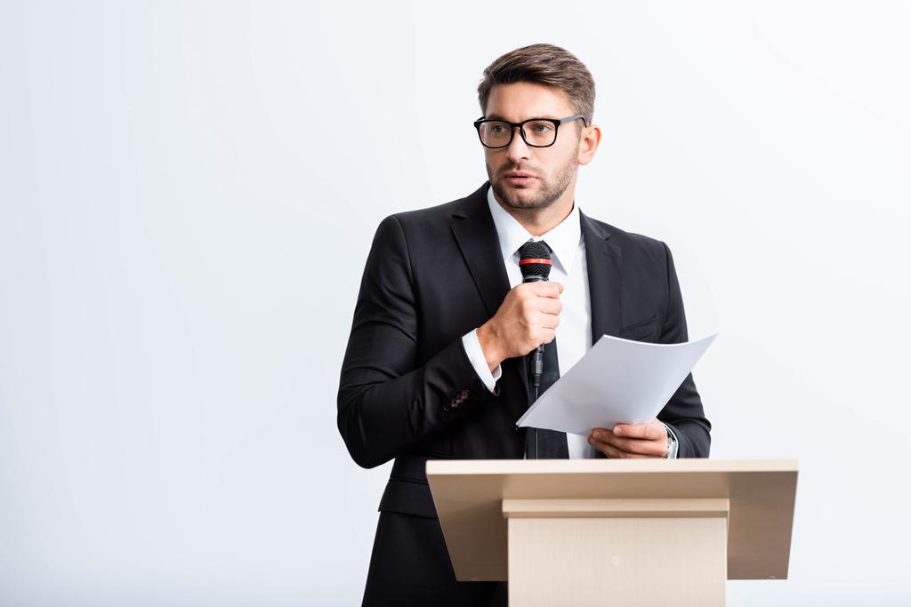 homem de negócios de terno em pé no tribuno pódio e falando durante conferência isolada em branco
  - Foto, Imagem
