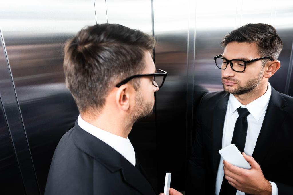 Hochwinkelaufnahme eines Geschäftsmannes im Anzug, der im Aufzug in den Spiegel schaut - Foto, Bild