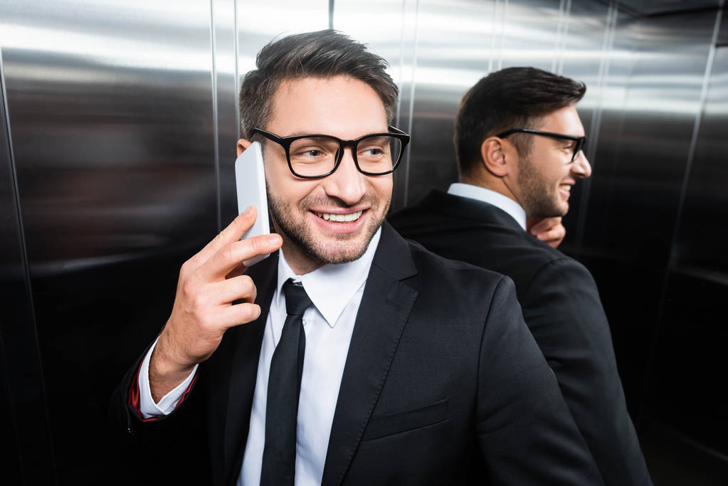uśmiechnięty biznesmen w garniturze rozmawiający na smartfonie w windzie - Zdjęcie, obraz