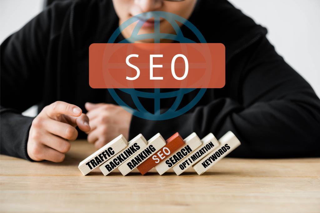 cropped view of seo manager pointing with finger and sitting near wooden rectangles with illustration of concept words of seo  - Photo, Image