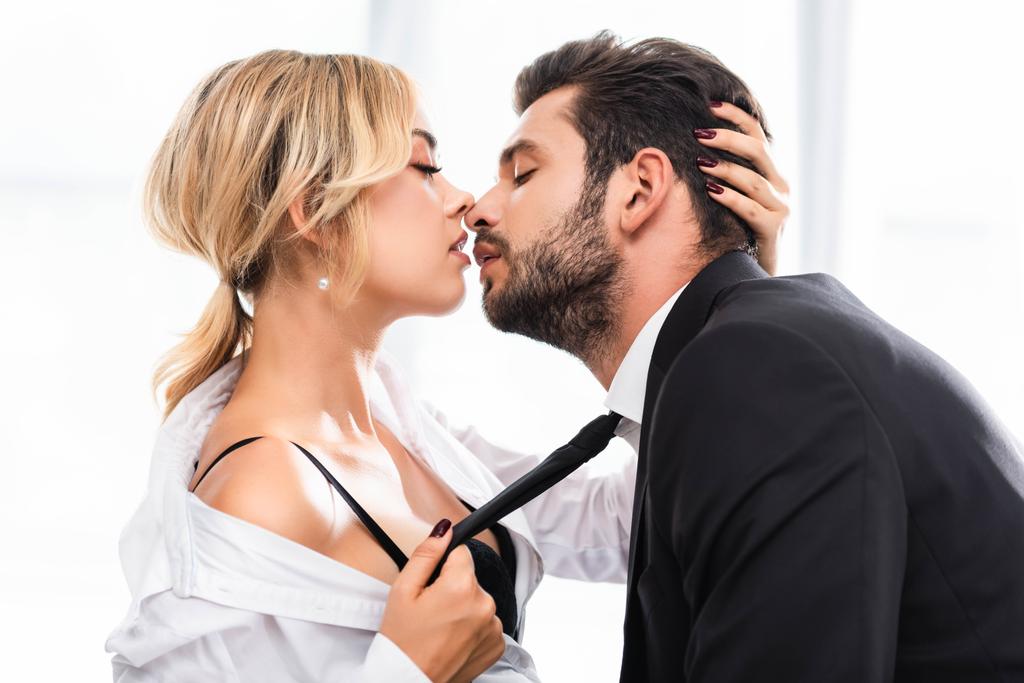 Side view of sexy businesswoman pulling colleague tie while flirting in office - Photo, Image