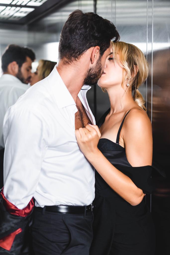 Üzletember leveszi a kabátját, miközben szexi nőt csókol az irodai liftben. - Fotó, kép
