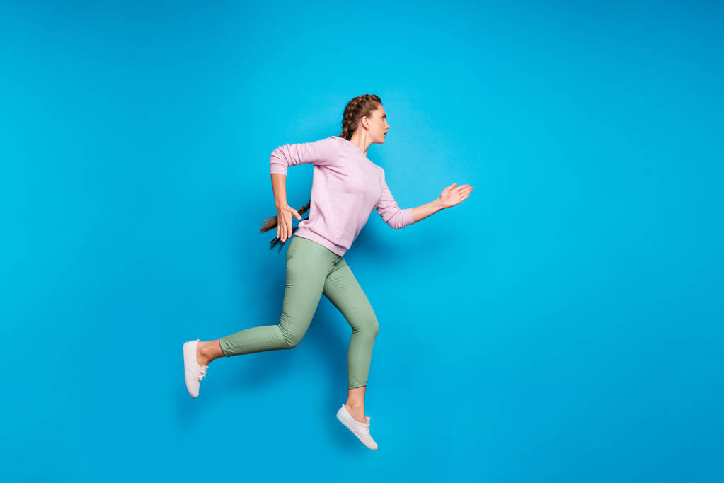Pełna długość profil zdjęcie ładna pani długie warkocze skoków wysokie zawody sportowe uruchomić, aby zakończyć linię nosić casual różowy pullover zielone spodnie odizolowane niebieski kolor tło - Zdjęcie, obraz
