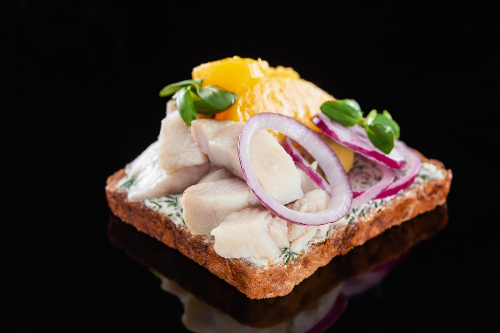 Nahaufnahme von Heringsfisch auf zubereitetem dänischen Smorrebrod-Sandwich auf schwarz  - Foto, Bild
