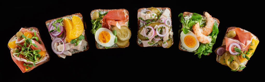 panoramatický záběr žitného chleba s připravenými dánskými sendviči smorrebrod izolovanými na černém  - Fotografie, Obrázek