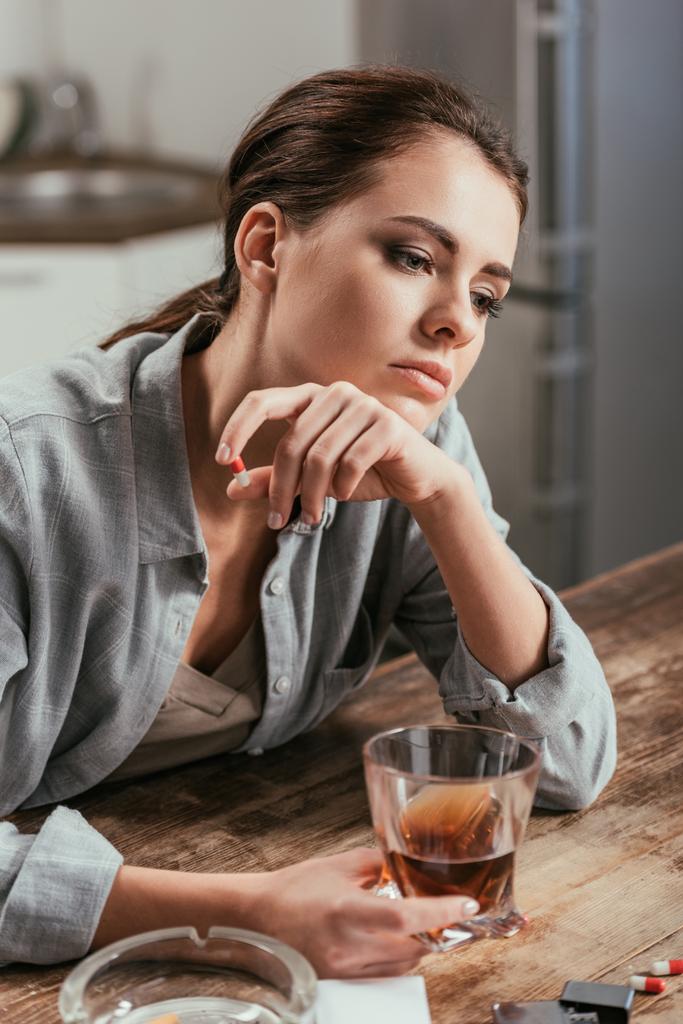 Alkol bağımlılığı olan endişeli kadın masada viski bardağı tutuyor. - Fotoğraf, Görsel