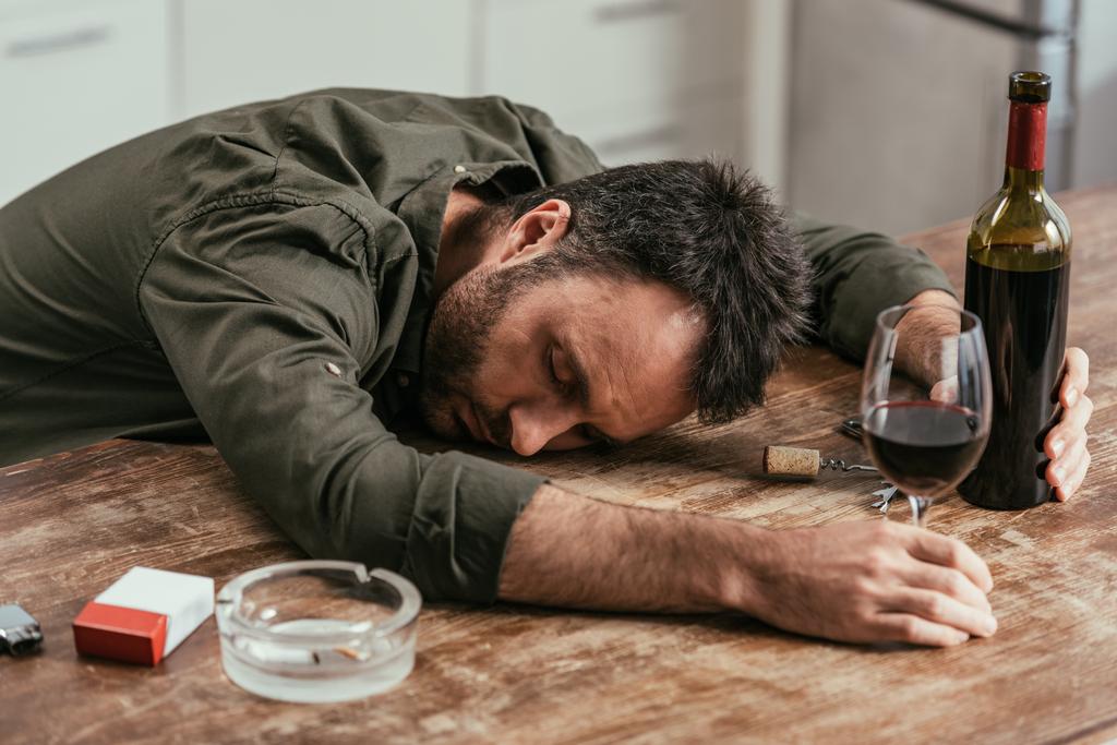 Pijany człowiek śpiący na stole z winem i papierosami - Zdjęcie, obraz